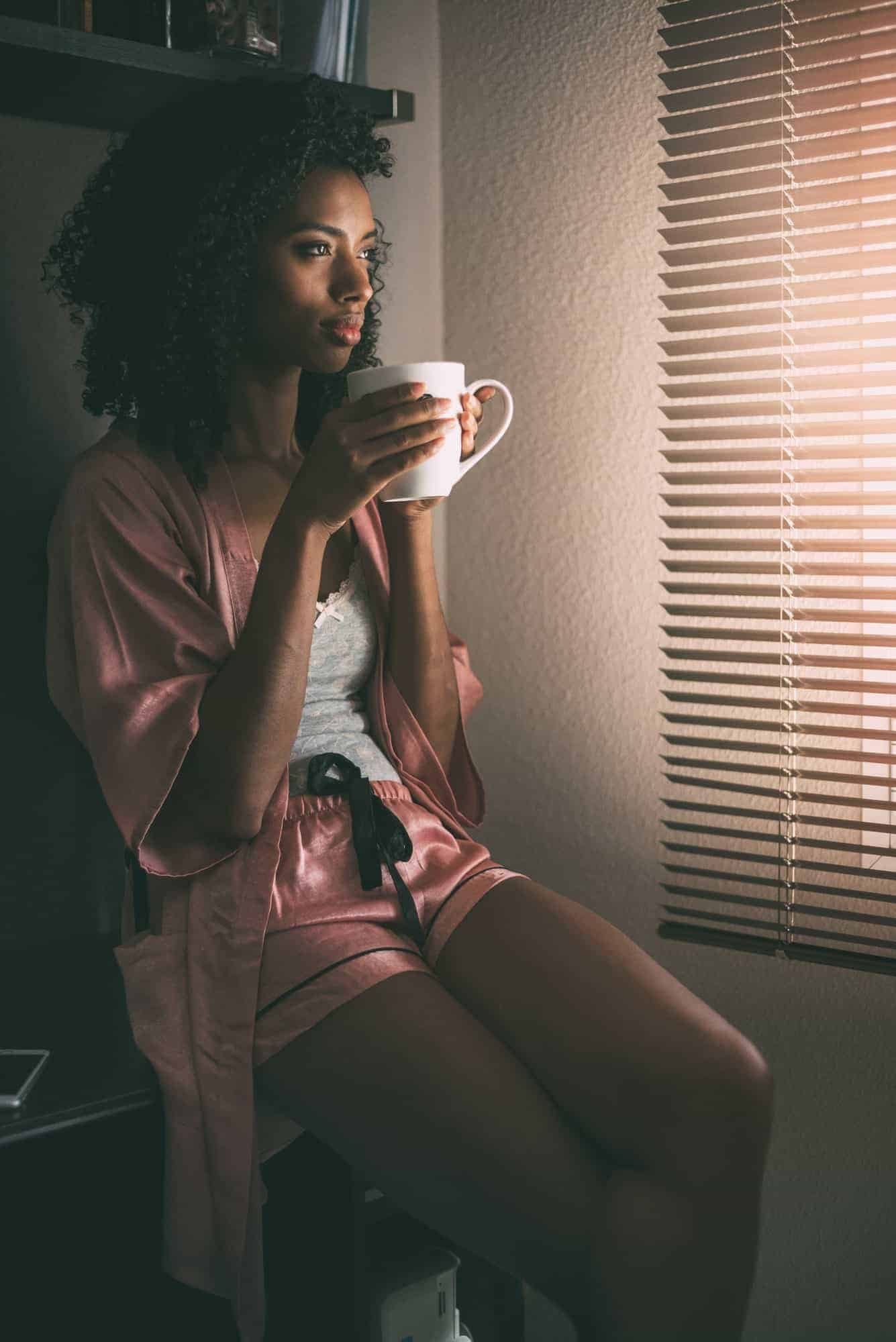 pretty black woman sitting at the window with cup of coffee