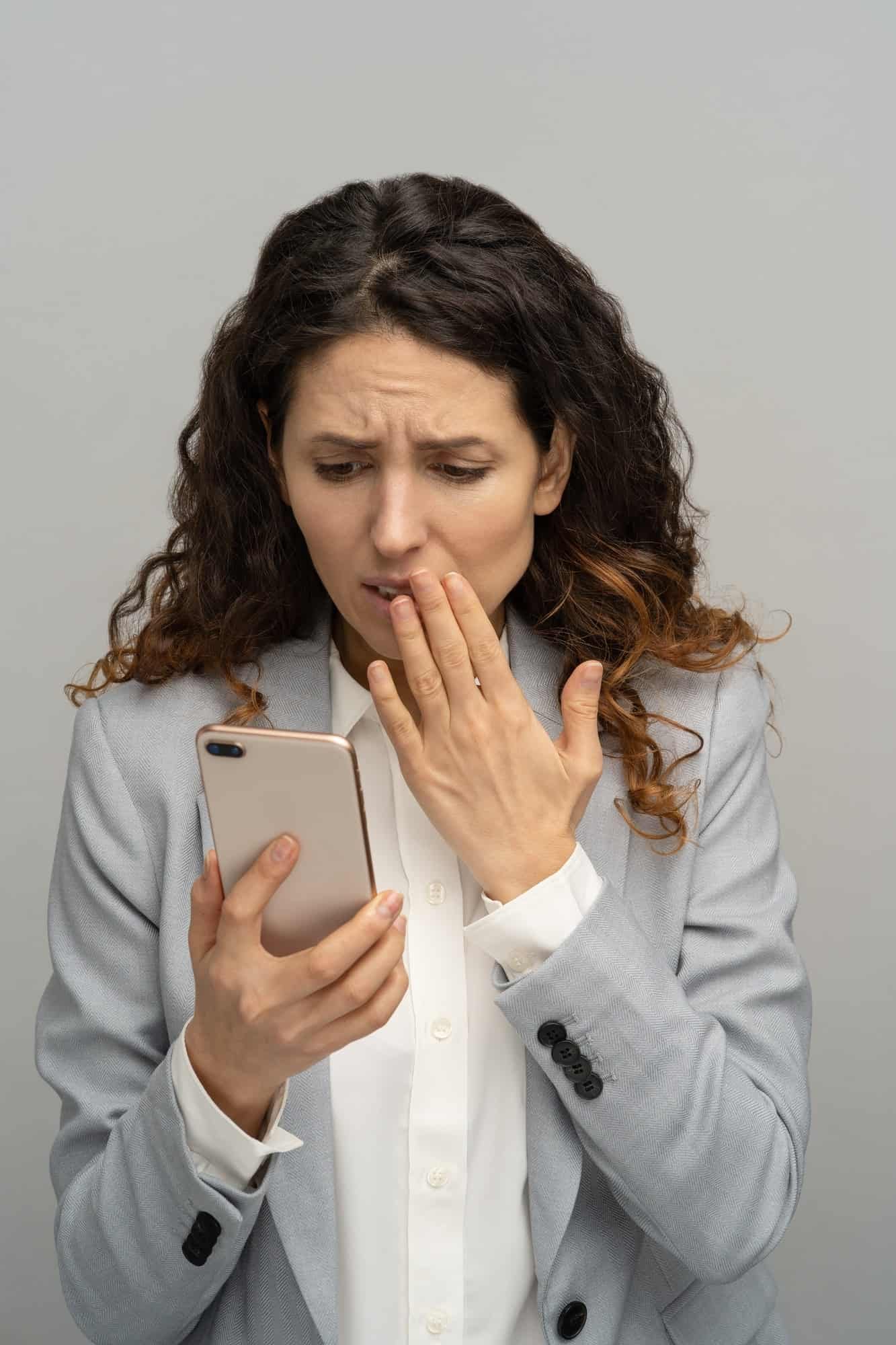 Frustrated shocked business woman or office worker looking at phone stunned with bad negative news