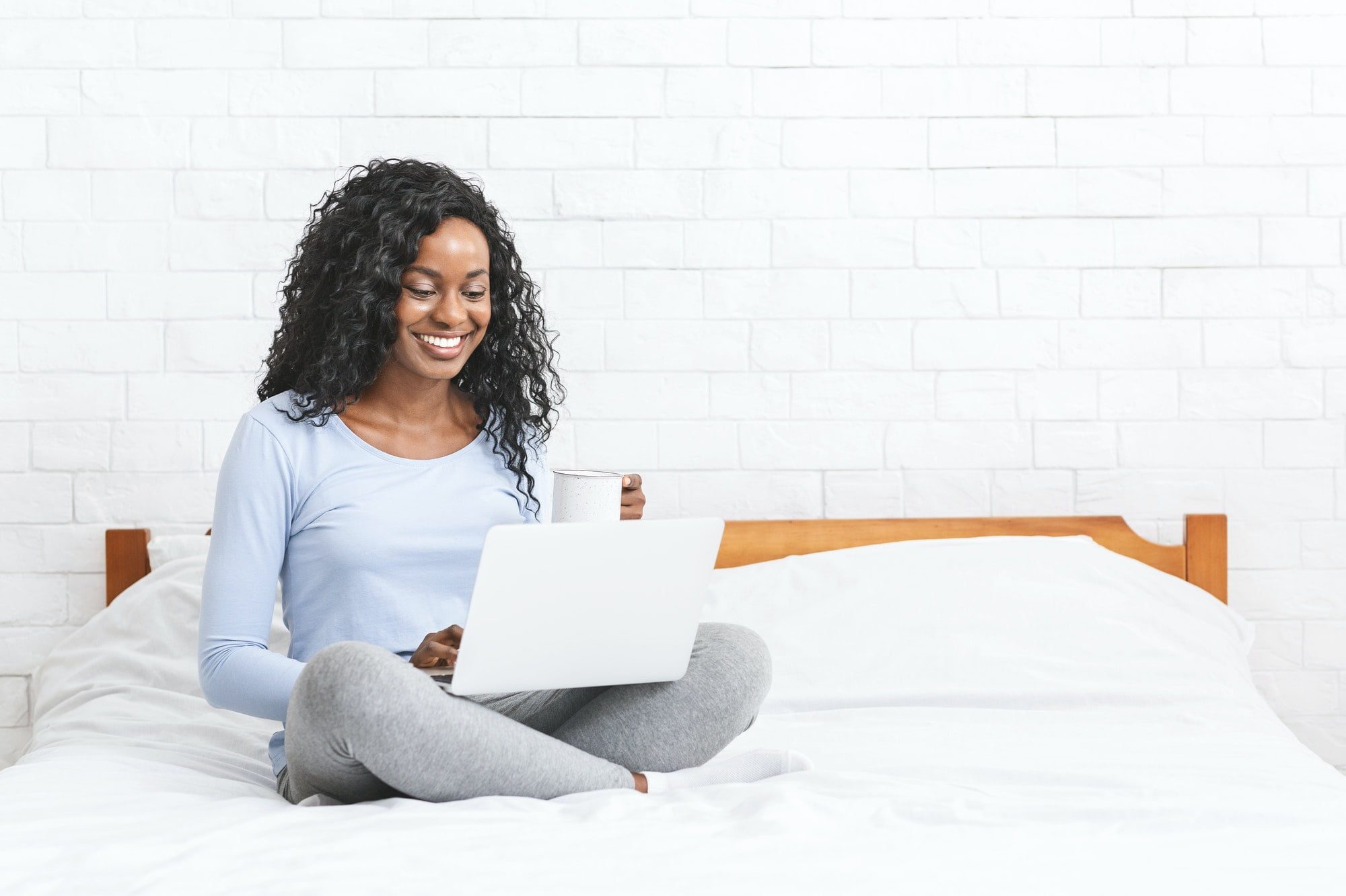 Beautiful smiling young woman sitting on bed, using laptop
