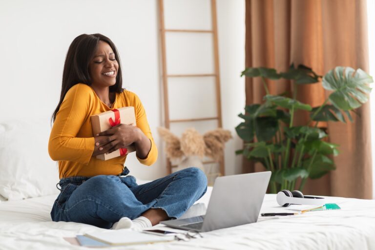 African Woman Hugging Gift Box During Video Call At Home