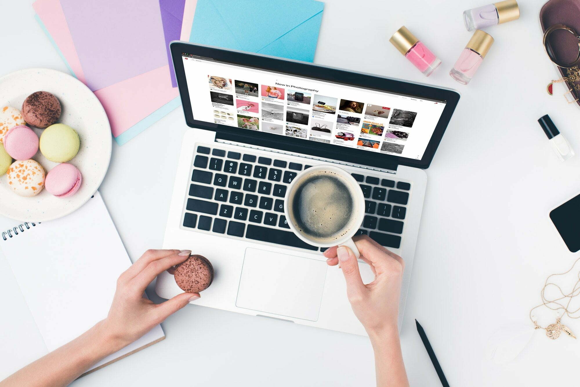 top view of woman drinking coffee with macaroon while using laptop with pinterest website