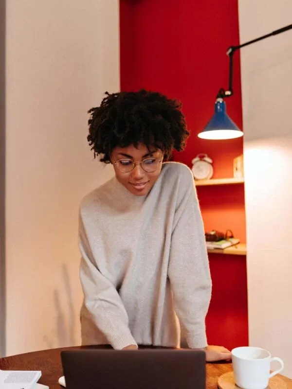 Girl in oversized sweater is standing near desktop and typing in laptop